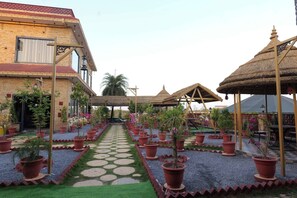 A courtyard with a central pathway, potted plants, and thatched-roof structures. - Surya Resort, Peaceful Stay with Modern Comforts (Chittorgarh)