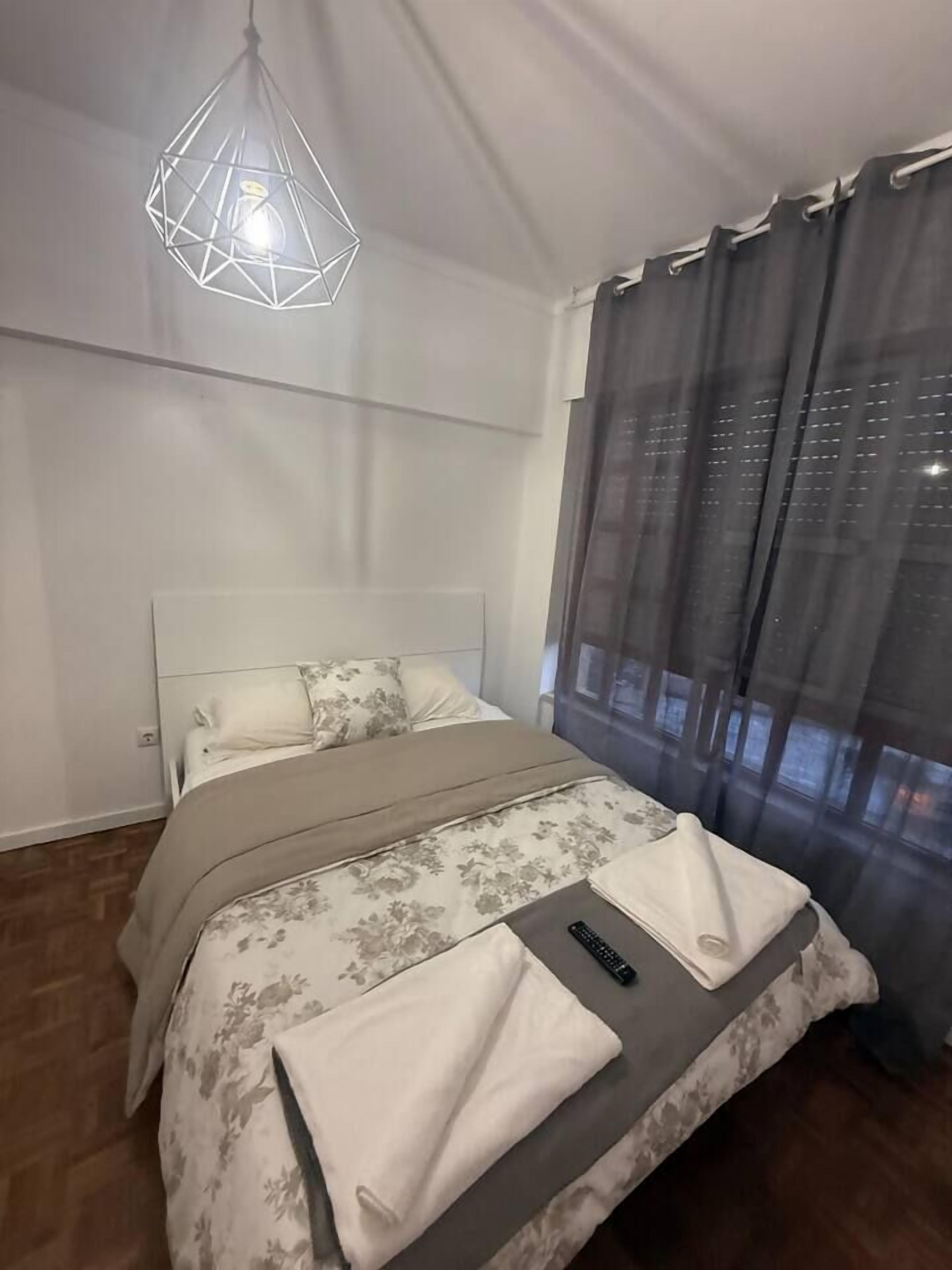 Ein Schlafzimmer mit einem Bett, einer Hängelampe und einem Fenster mit Vorhängen.