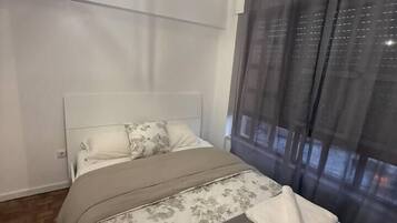 Ein Schlafzimmer mit einem Bett, einer Hängelampe und einem Fenster mit Vorhängen.