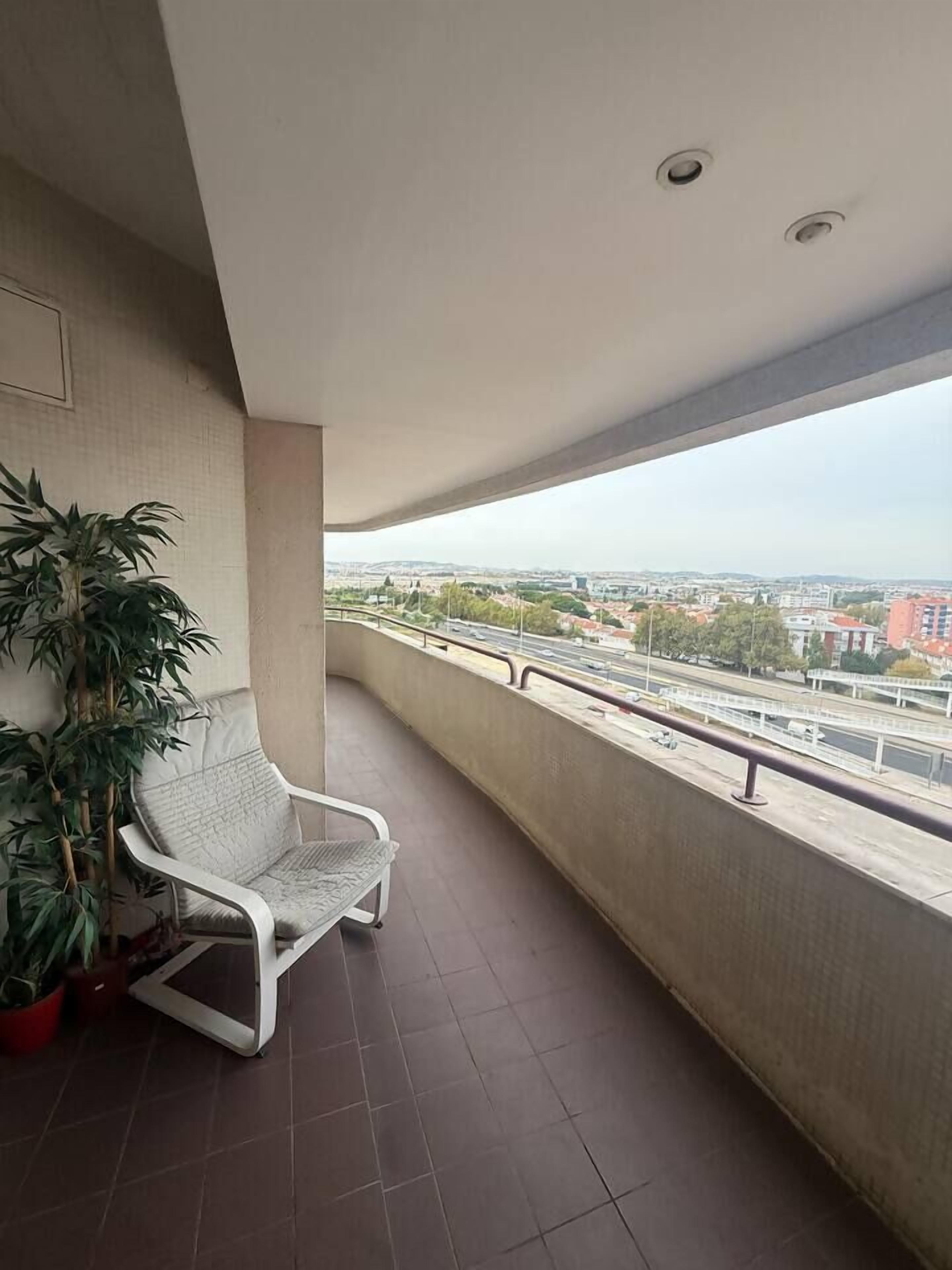 Ein Balkon mit einem weißen Stuhl, einem Topfpflanzen und Blick auf eine Stadtlandschaft.