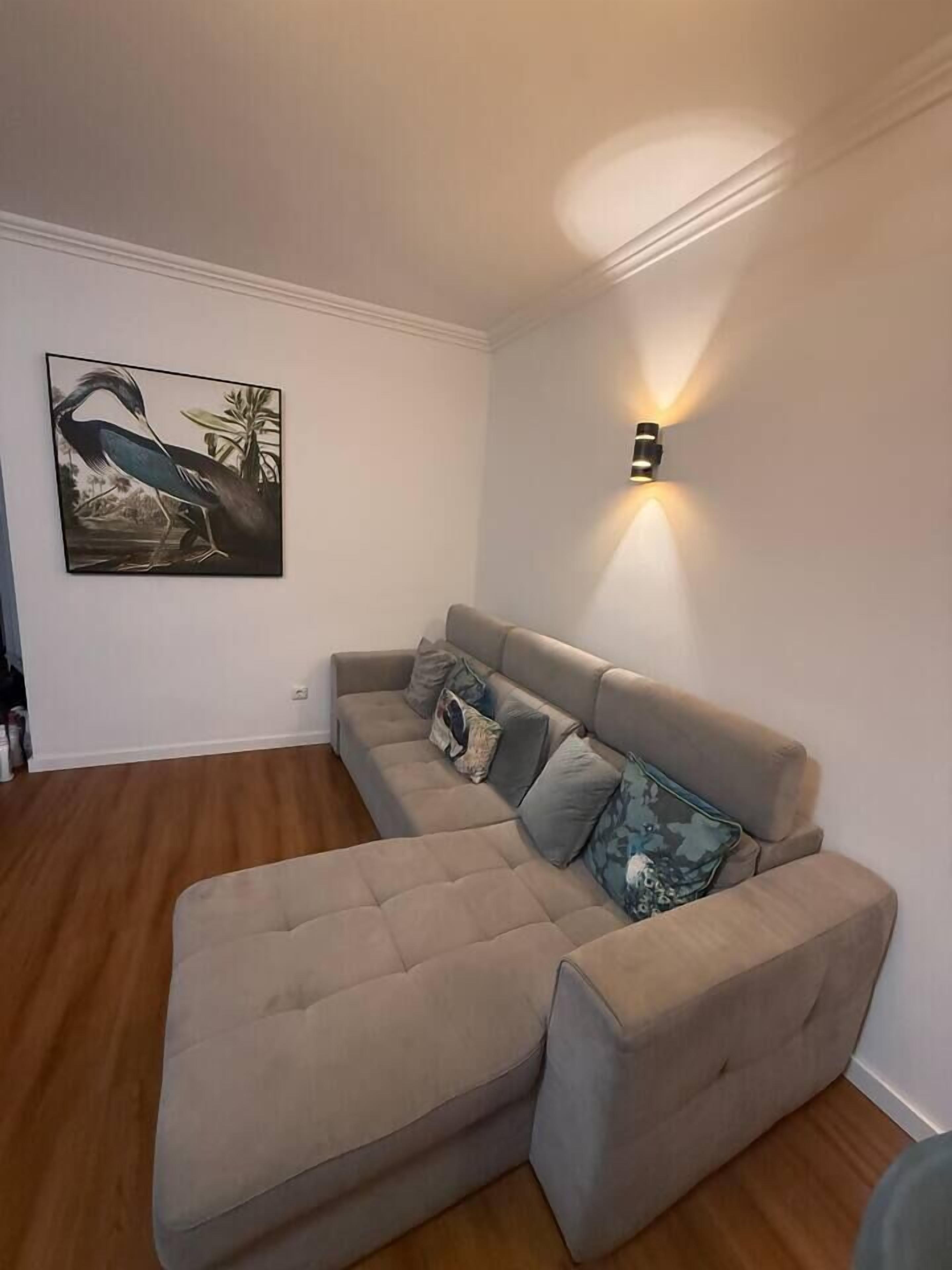 Ein Ecksofa mit einer Wandleuchte und einem gerahmten Bild.