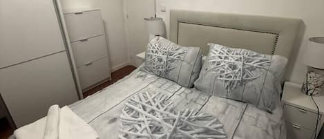 A bedroom with a bed, a nightstand, a lamp, and a wardrobe.