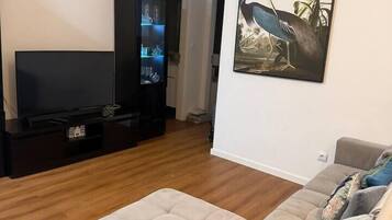 Ein Wohnzimmer mit Flachbildfernseher, einer dunklen Unterhaltungsecke, einem beigen Sofa und einem gerahmten Wandbild mit Tierdarstellungen.