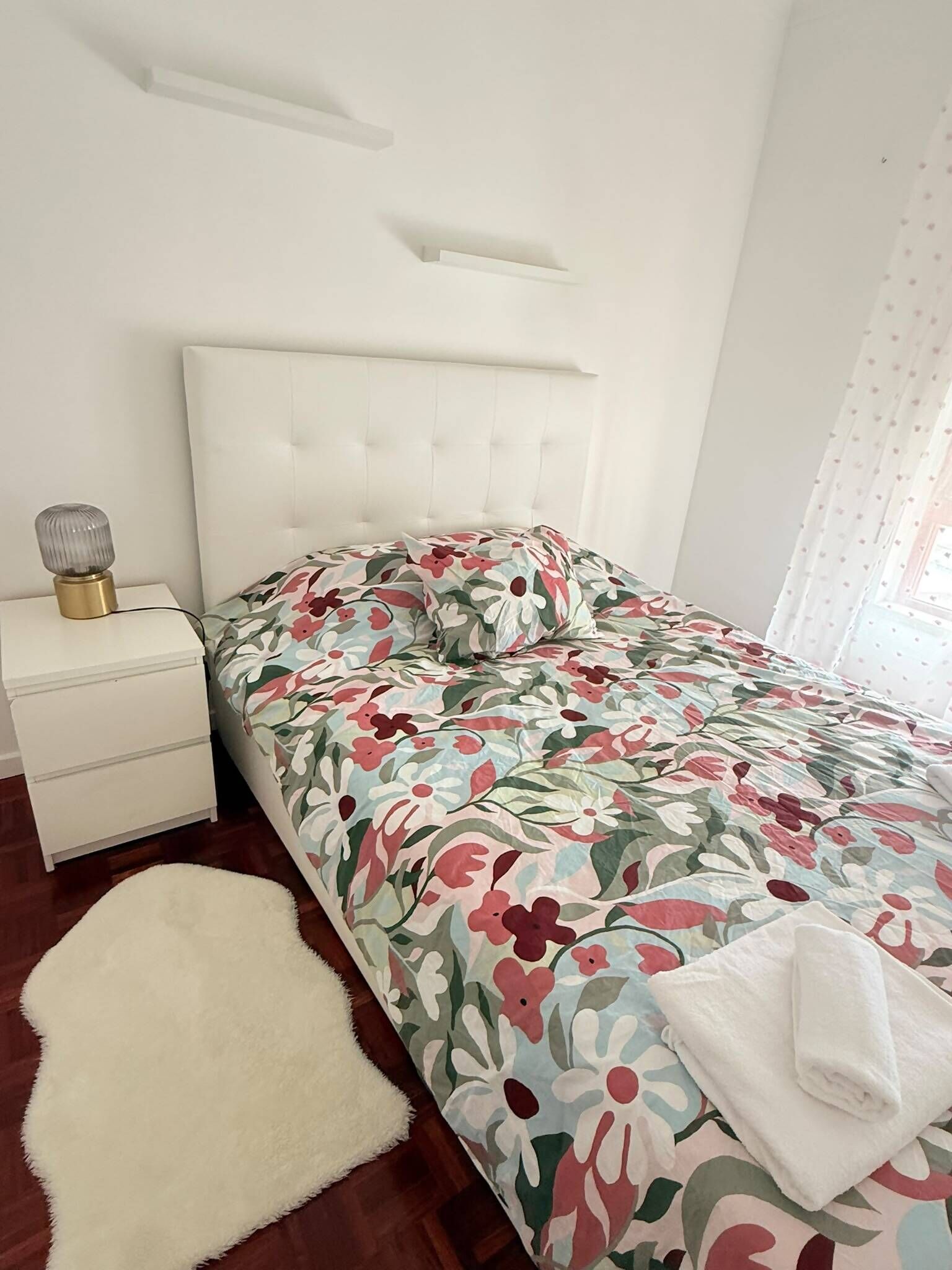 Ein Schlafzimmer mit einem Bett, einem Nachttisch, einer Lampe und einem weißen Teppich.