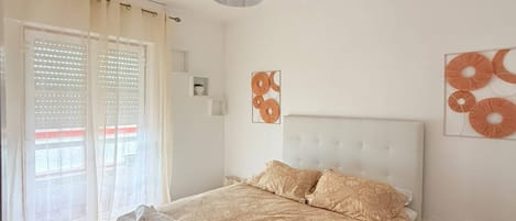 A bedroom with a bed, a hanging lamp, a window with blinds, and wall art.