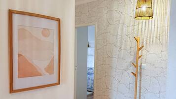 Ein Korridor mit Holzboden, einem gerahmten abstrakten Gemälde, einer strukturierten Wand und einer Stehlampe.