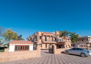 A hotel with a checkered pavement entrance, a gated driveway, and a white car parked nearby. - Hotel Ramdev (Pokhran)