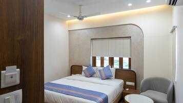 A hotel room with a bed, bedside table, chair, and a window with blinds.