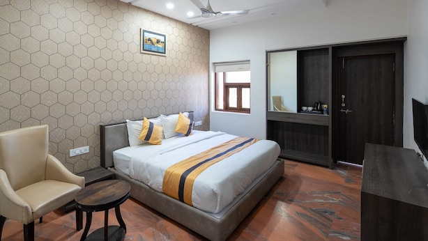 Una habitación de hotel con cama, una silla, una mesita, un armario y televisor.