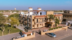Un edificio residencial de varios pisos con entrada porticada, zona de estacionamiento y torre de agua al fondo.