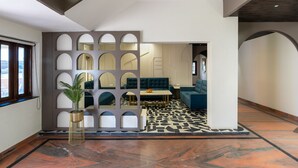 Un interior moderno con piso estampado geométrico, un área de estar con sofá y mesa, y una pared decorativa con círculos recortados.