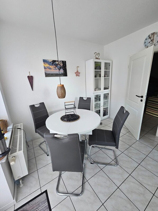 A dining area with a round table, four chairs, a cabinet, and a clock on the wall.