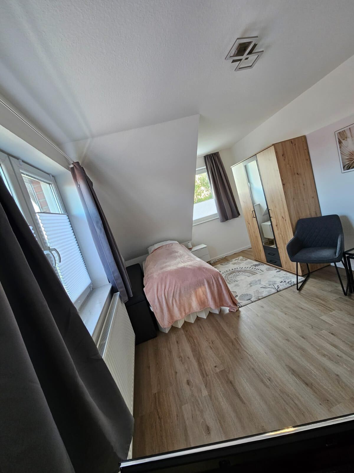 A bedroom with a bed, a chair, a wardrobe, and a window.