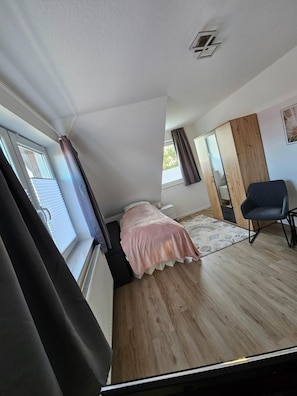 A bedroom with a bed, a chair, a wardrobe, and a window.