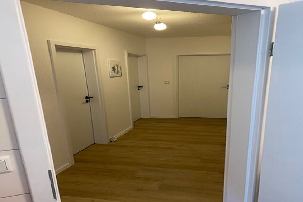 A hallway with wooden flooring and white walls, leading to closed doors.