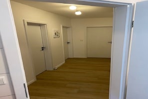 En hall med trägolv och vita väggar, som leder fram till stängda dörrar.