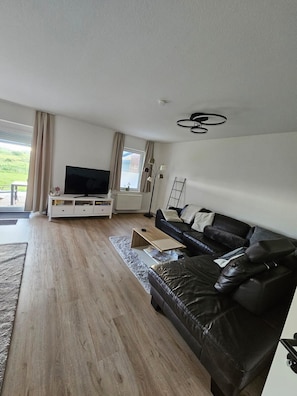 A modern living room with a black leather sofa, a flat-screen TV, and a wooden floor.