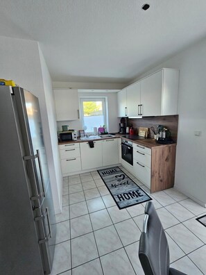 A modern kitchen with white cabinets, a stainless steel refrigerator, a wooden countertop, and a kitchen island.