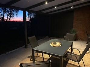 An outdoor patio with a table and chairs, a potted plant, and a view of the sky.