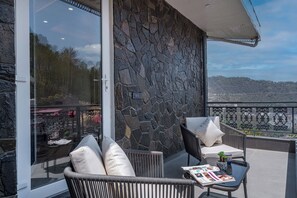 Un balcón con mobiliario de mimbre, un muro de piedra y vista a un paisaje urbano.