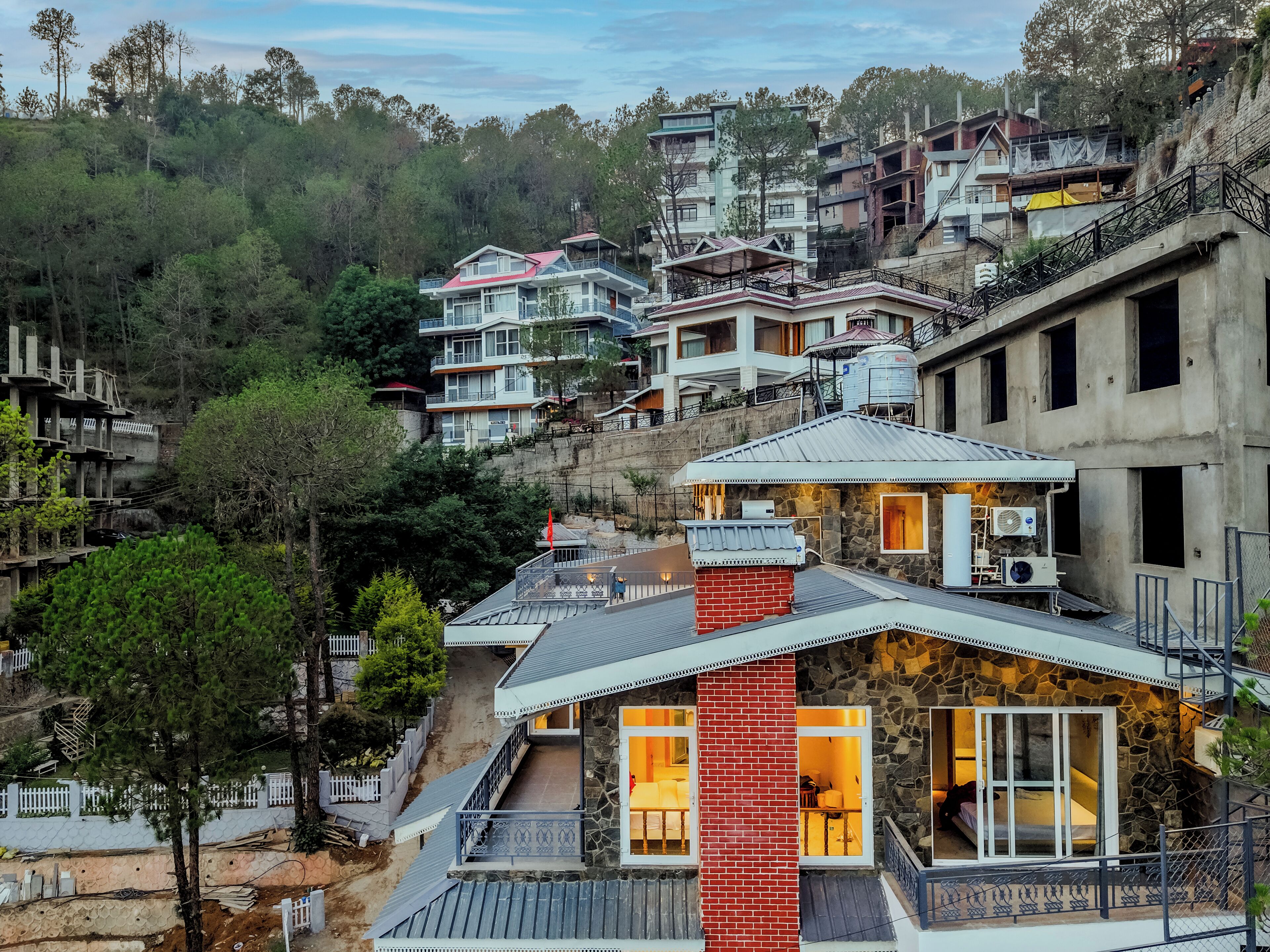 Un quartier résidentiel situé sur une colline, composé de plusieurs maisons, dont une demeure imposante avec une façade en pierre et une cheminée en briques rouges.