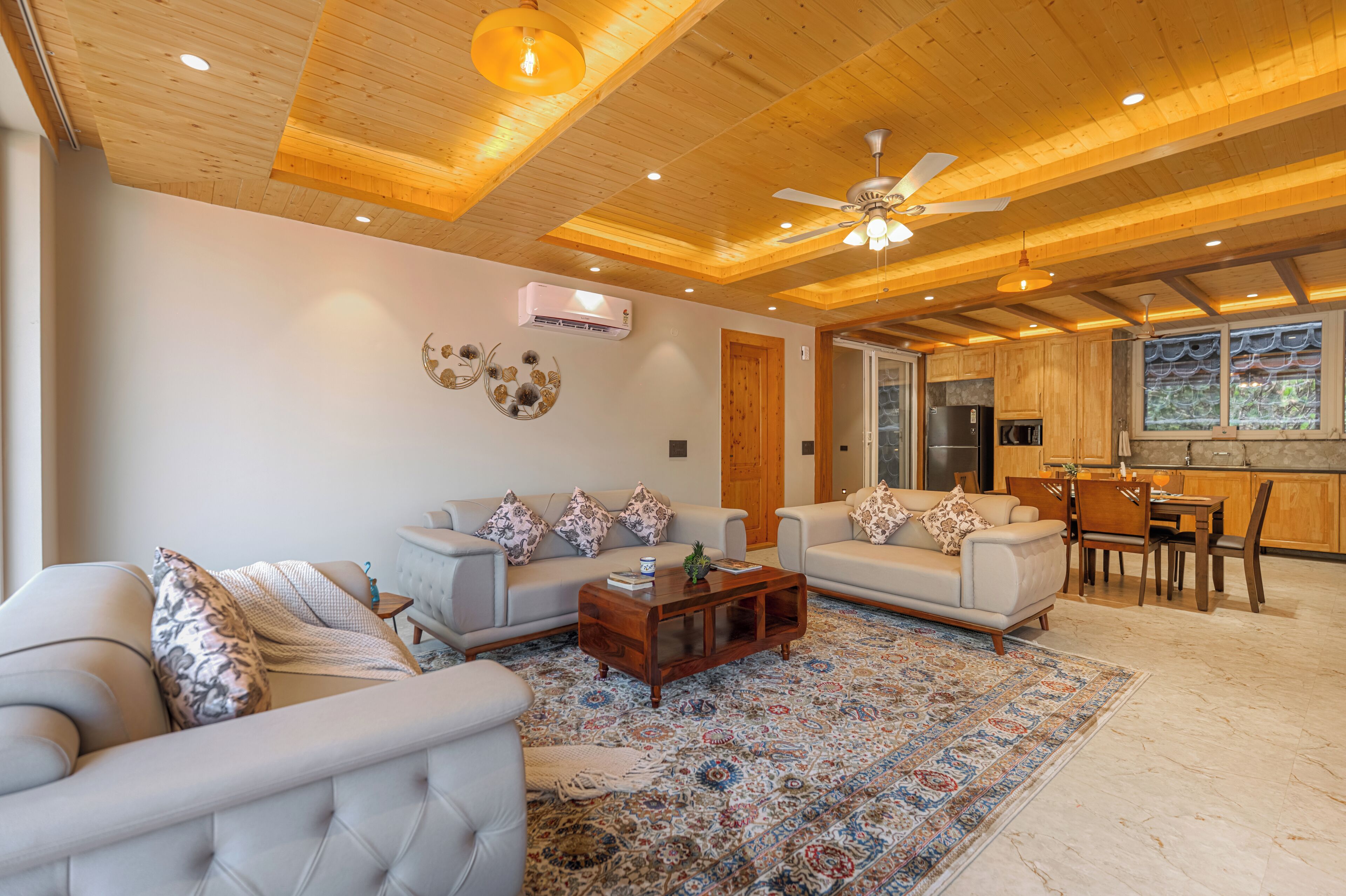 Un salón amplio con techo alto, vigas de madera, ventilador de techo y un ventanal con vistas al exterior.