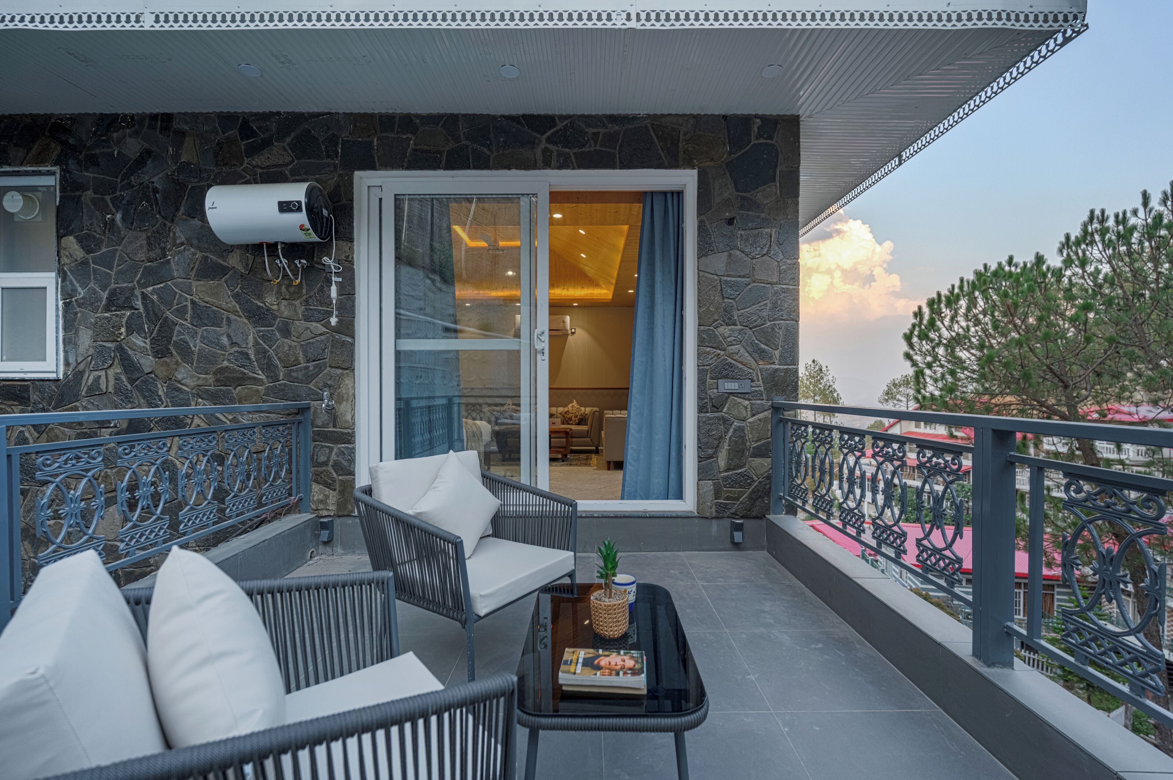 A balcony with wicker furniture, a table with a book and a plant, and a stone wall with a door leading to an interior space.