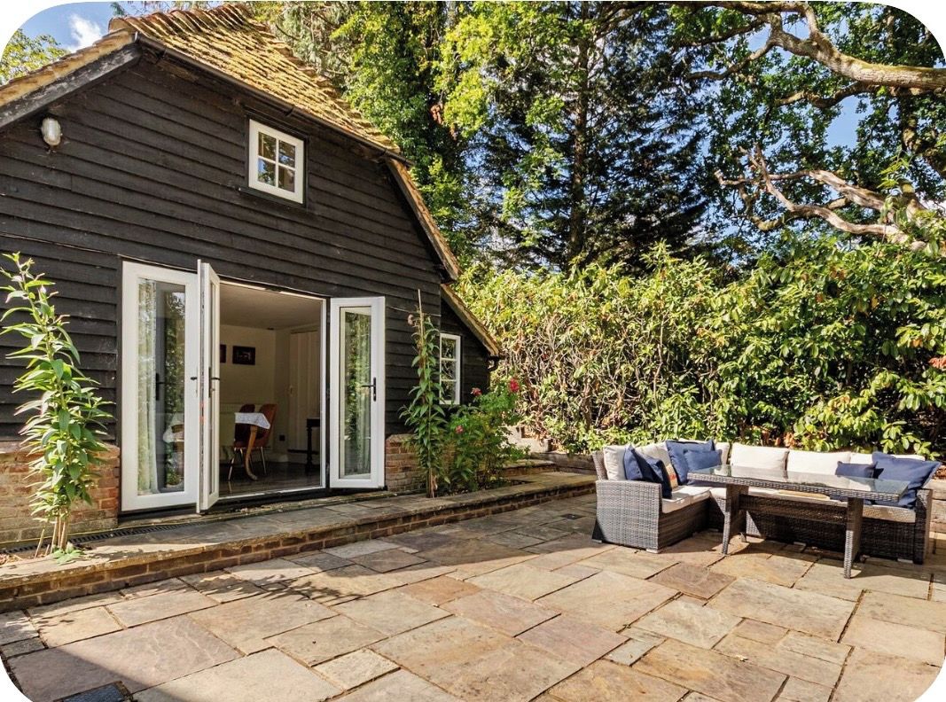 A wooden cottage with a glass door entrance, a stone patio, and outdoor furniture.
