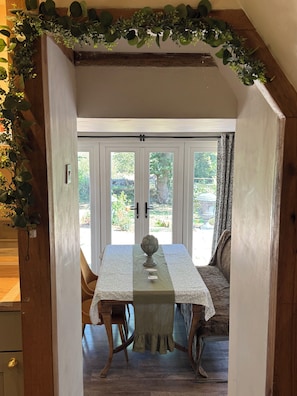 A dining area with a table set for two, a vase centerpiece, and a view of the outdoors through large doors.