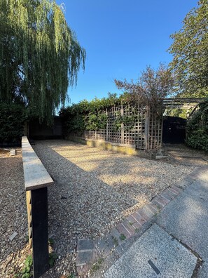 A gravel patio with a wooden bench, a wooden fence, and a weeping willow tree.