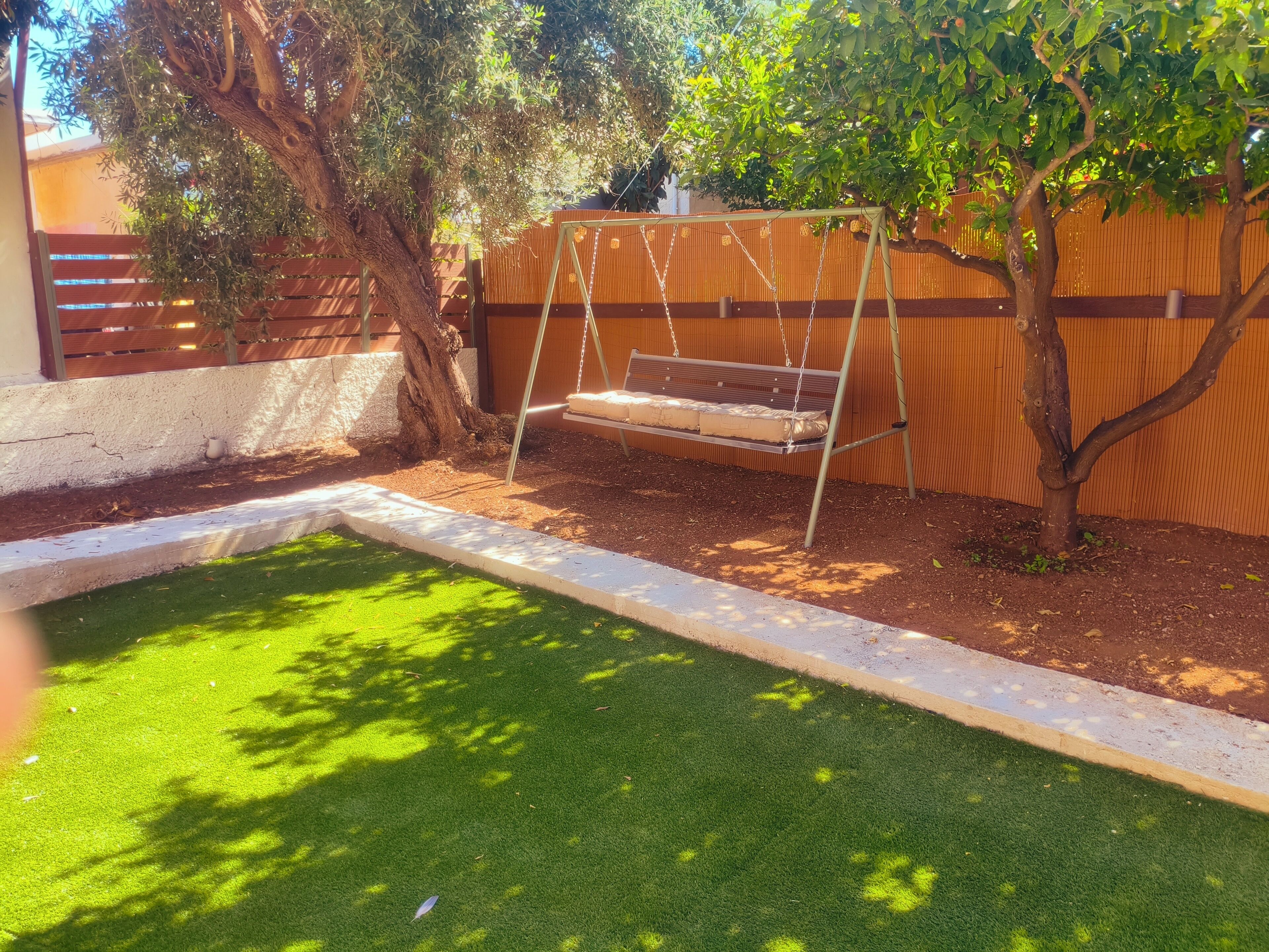 A backyard with a swing set, a small pool, and a tree.