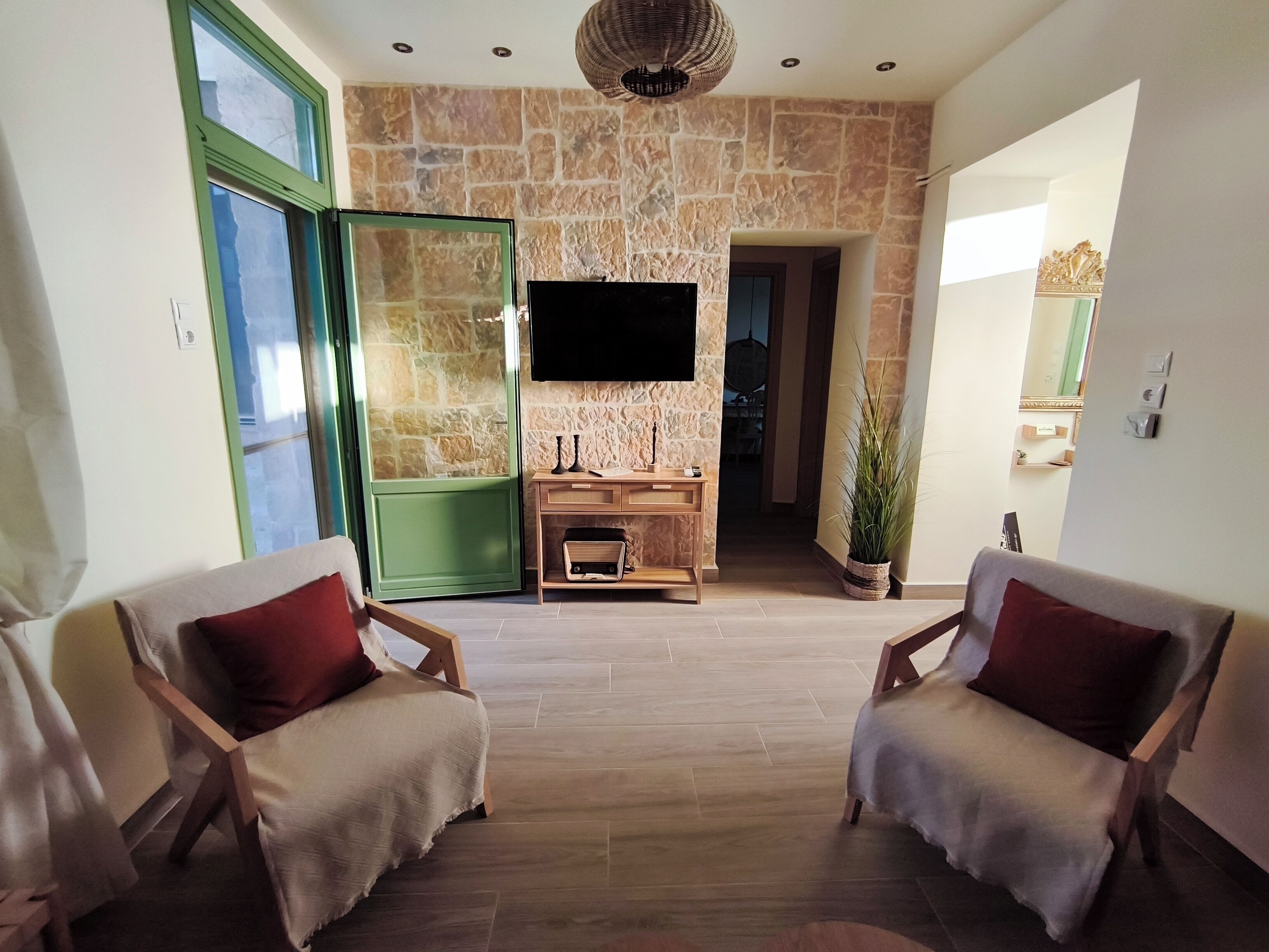 A living room with a stone wall, a flat-screen TV, a wooden console table, and two armchairs.