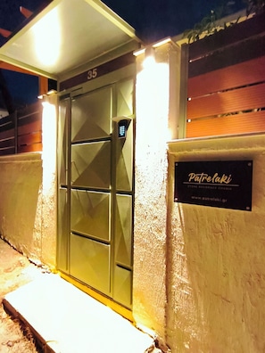 A building entrance with a numbered door, a sign with a website address, and a stone residence label. - Patrelaki Stone Residence Chania, with private yard (Chania)