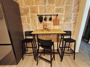 A kitchen with a stone wall, a wooden table, four black chairs, and a hanging pot rack with potted plants. - Patrelaki Stone Residence Chania, with private yard (Chania)