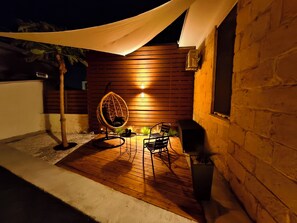 Une terrasse avec un fauteuil suspendu, une table et un barbecue.