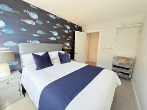 A bedroom with a bed, a nightstand, a lamp, a wall with fish patterns, and a door leading to another room. - Modern 2‑Bed Apartment with Balcony, Super‑King Bed & 50m to Swanage Beach (Swanage)