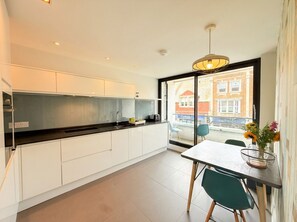 A modern kitchen with white cabinets, a black countertop, and a dining area with a table and chairs. - Modern 2‑Bed Apartment with Balcony, Super‑King Bed & 50m to Swanage Beach (Swanage)