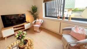Una sala de estar con un televisor de pantalla plana, un sofá, una silla, una mesa de centro con aperitivos y una ventana con persianas.
