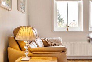 Une pièce avec un canapé, une lampe, une fenêtre avec une mangeoire à oiseaux et un radiateur.