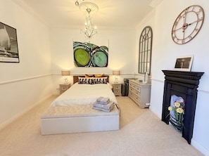 Une chambre à coucher avec un grand lit, un lustre, une cheminée décorée de fleurs et des œuvres d’art accrochées aux murs.