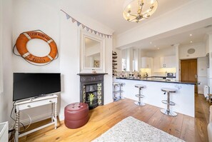 Ein modernes Wohnzimmer mit Flachbildfernseher, Kamin, Hocker in Rot und einer Küchenzeile mit Bar.
