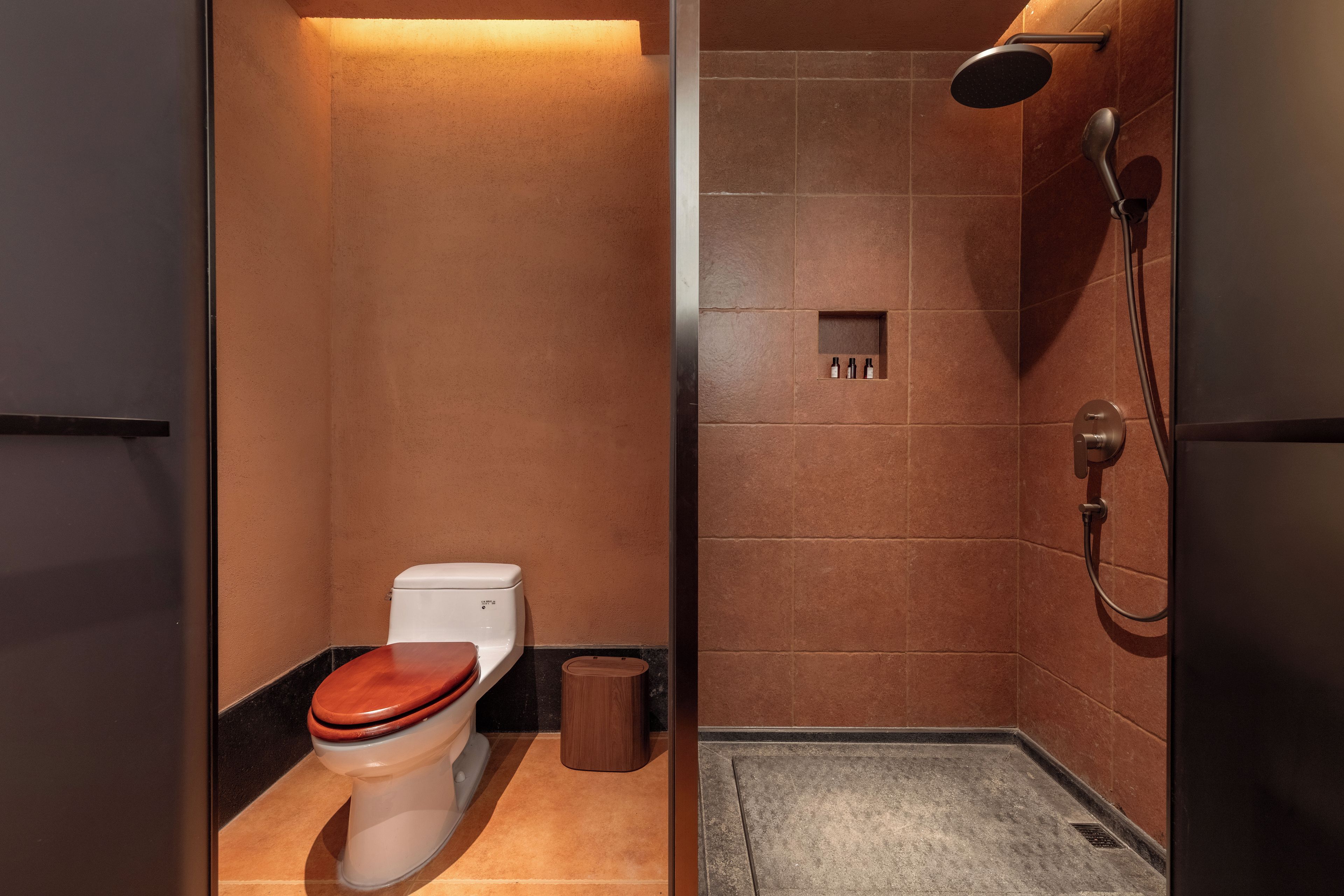 A bathroom with a toilet, a shower, and a small shelf with toiletries.