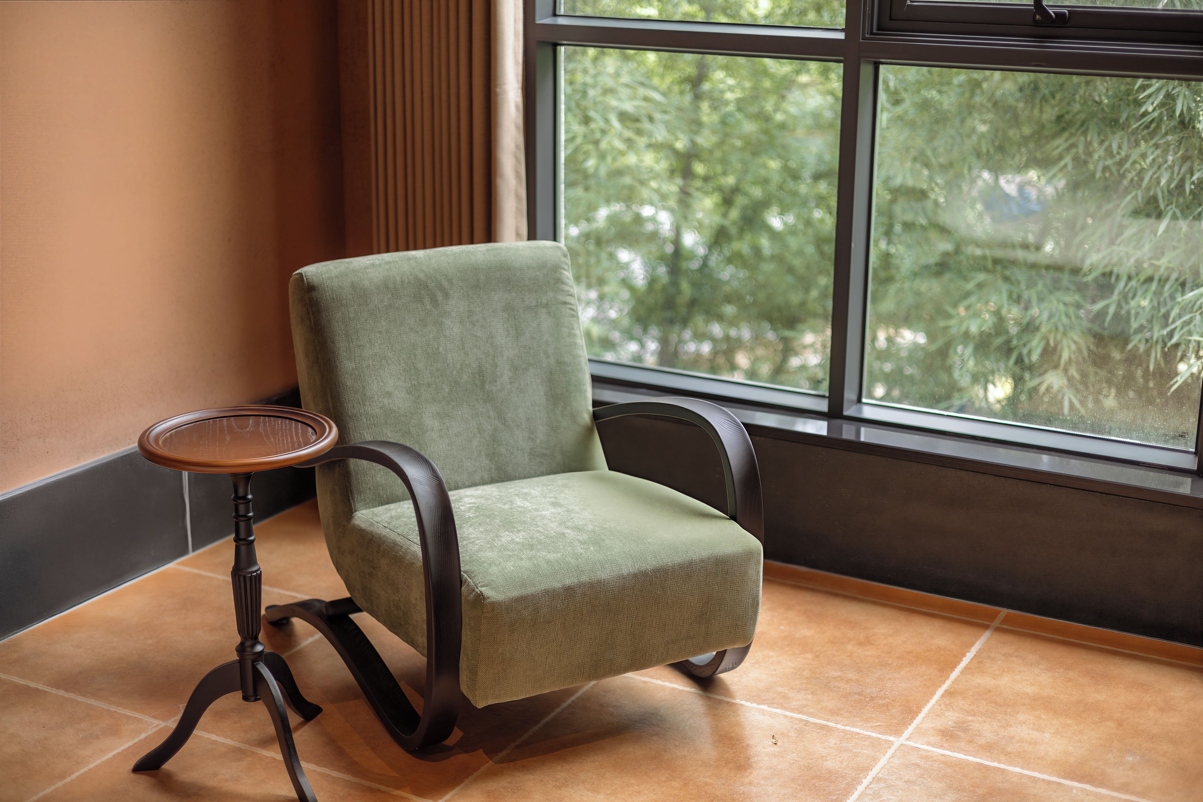 A chair with a wooden side table, positioned near a window with a view of greenery outside.