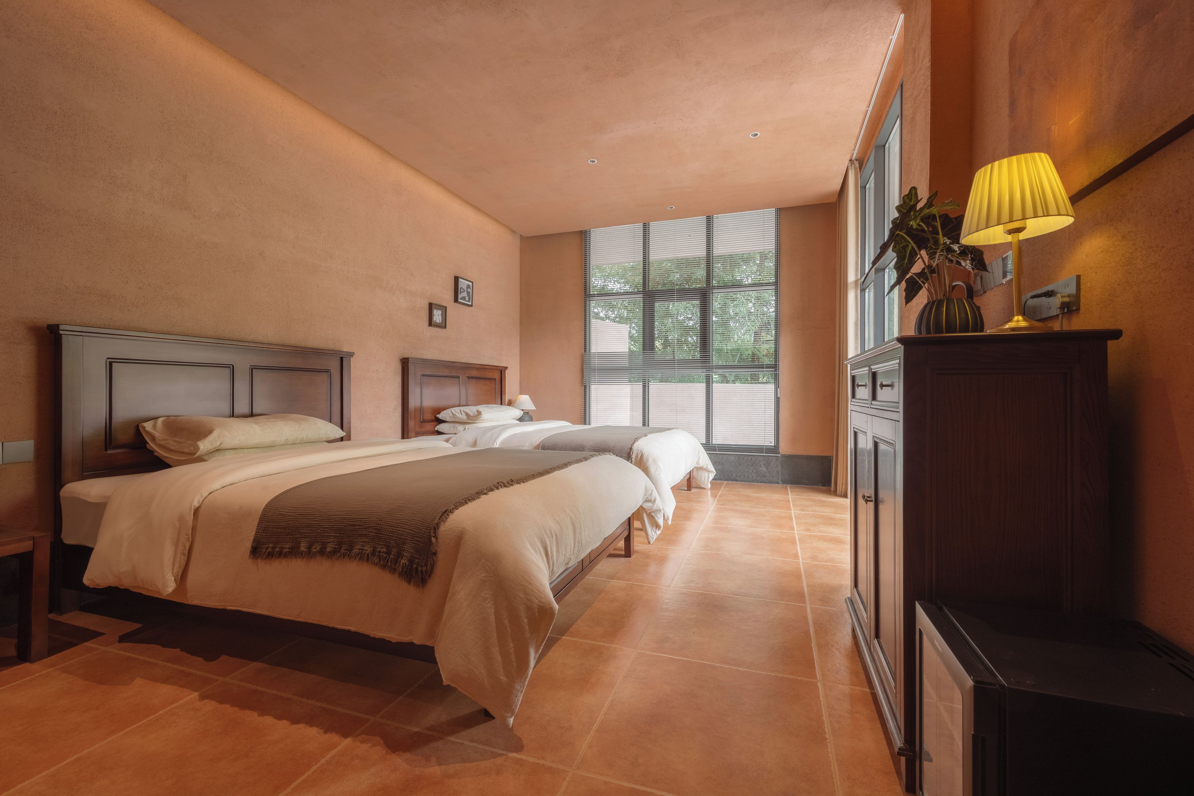 A hotel room with two beds, a nightstand, a lamp, and a view of the outdoors.