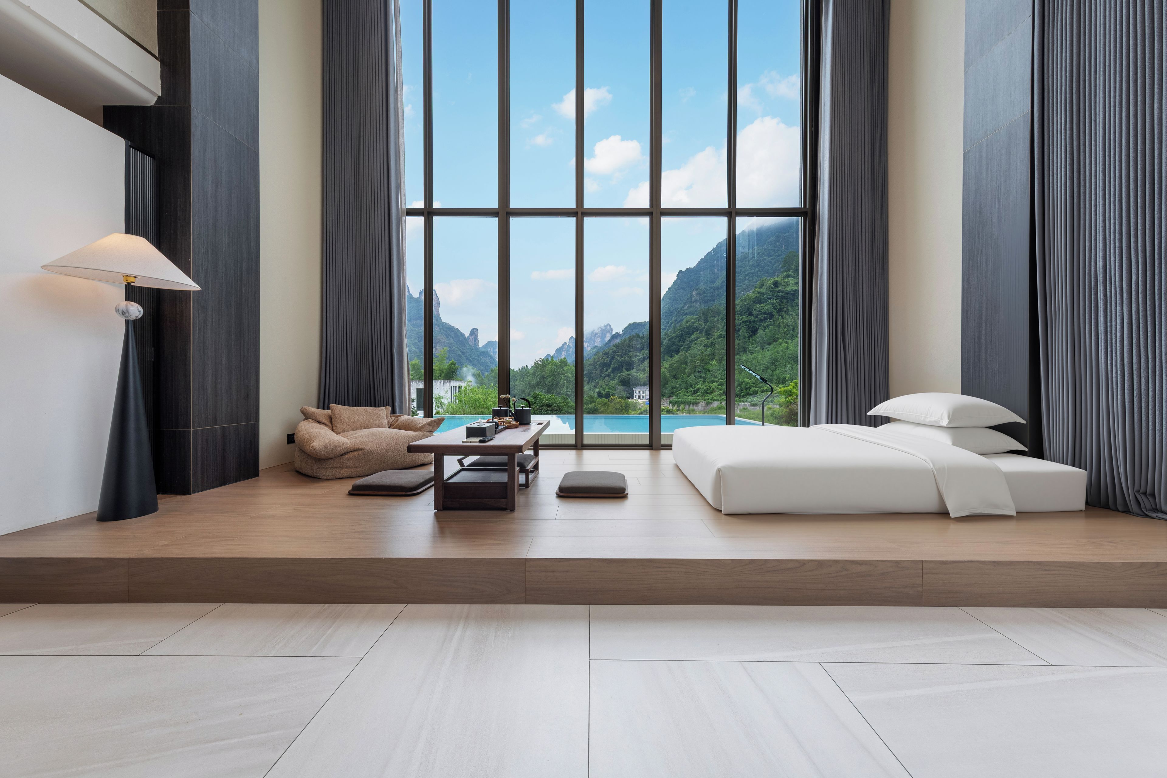A modern room with a large window, a sofa, a table, and a lamp.