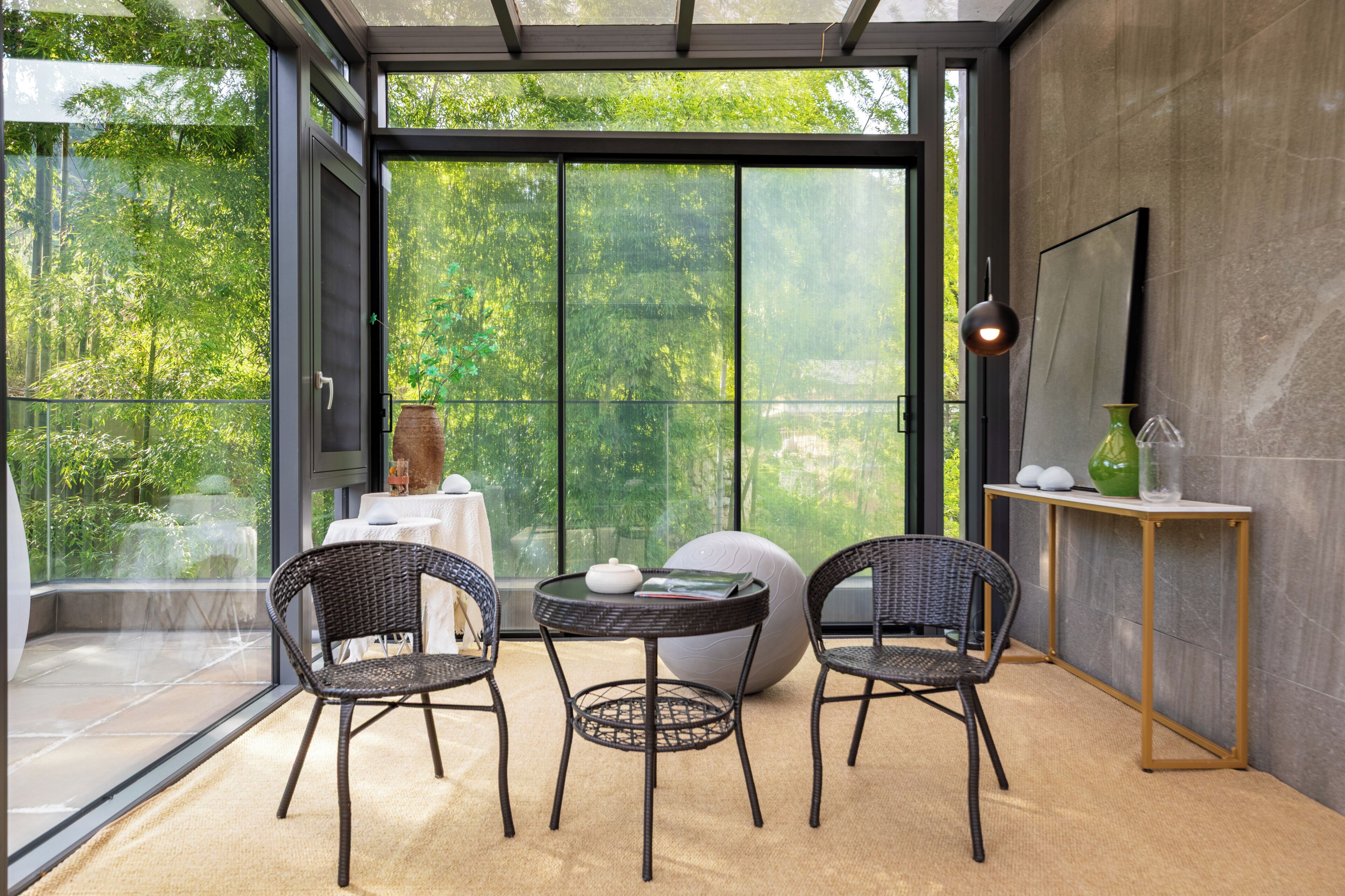 Un interior moderno con un ventanal que da a un balcón, muebles de mimbre, una mesa redonda y una decoración minimalista.