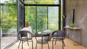Un interior moderno con un ventanal que da a un balcón, muebles de mimbre, una mesa redonda y una decoración minimalista.