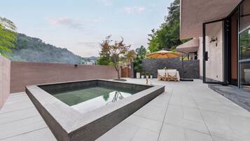 A modern outdoor pool area with a stone border, a wooden deck, and a seating area with a table and chairs.