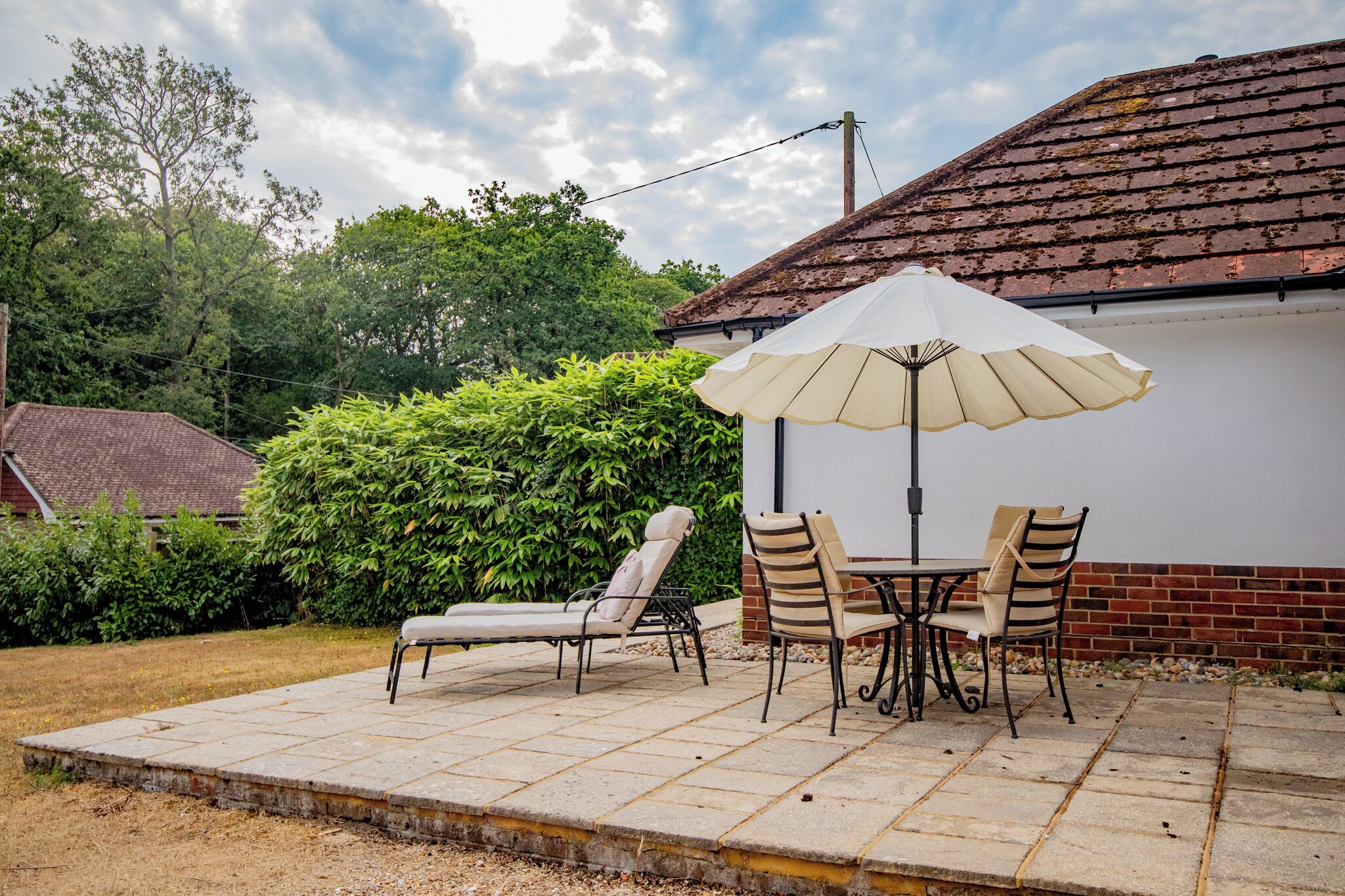 An outdoor patio with a table and chairs, a large umbrella, and a brick wall.