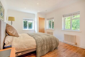 A bedroom with a bed, two windows, a radiator, and a door. - Kuldana - A Peaceful South Downs Retreat (Storrington)